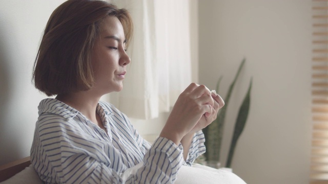 一个亚洲女人得了流感，坐在床上用纸巾打喷嚏视频素材