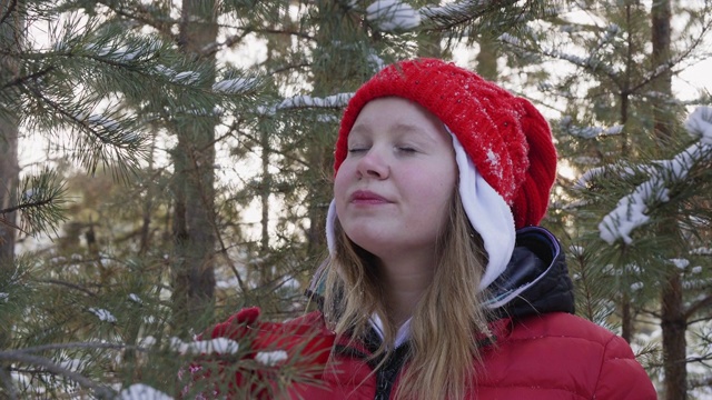 快乐的年轻女子享受热茶在雪山冬季森林假日散步。肖像美丽的女孩在红帽子喝茶在冬天的林地背景。视频素材