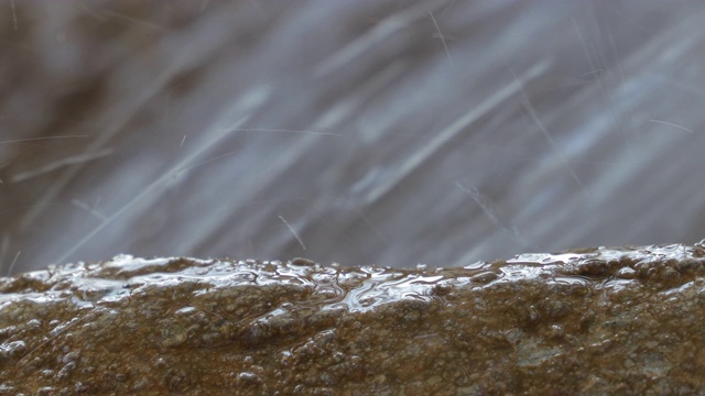 水滴落在石头表面，背景是湍急的水流。特写镜头视频素材