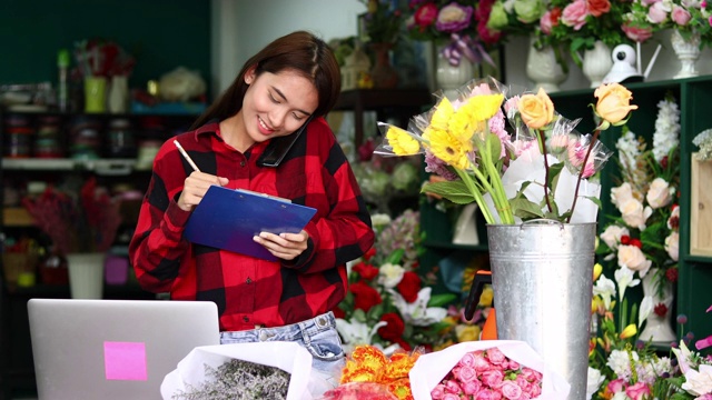 亚洲妇女花店小生意花店老板和她正在用她的电话和笔记本电脑为她的商店接受订单。视频素材