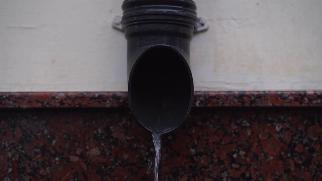 雨水从雨水排水管在建筑物墙壁上流动的特写。视频素材