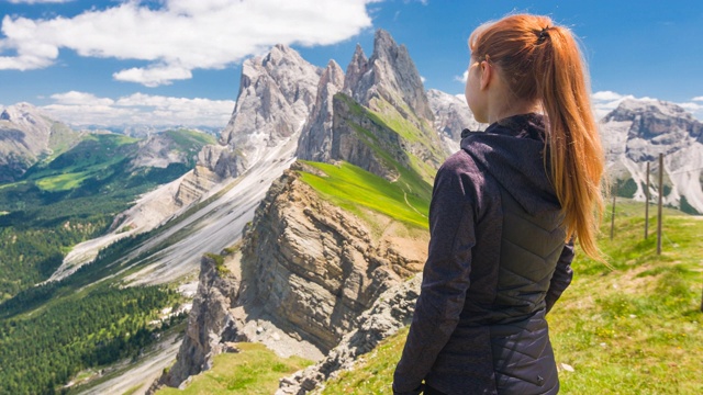 女游客探索山坡，站在山顶，欣赏周围的壮丽的山在一个美丽的阳光灿烂的日子视频素材