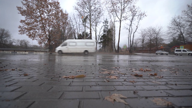 秋天的雨天，城市交通在潮湿的道路上行驶，汽车驶过一个车轮溅起水花的水坑。视频素材