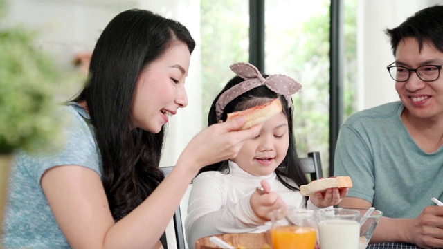 幸福亚洲日本家庭早餐在家。清晨，年轻的父母和女儿在厨房的桌子上吃麦片喝橙汁。品质时刻结合家庭理念理念视频素材