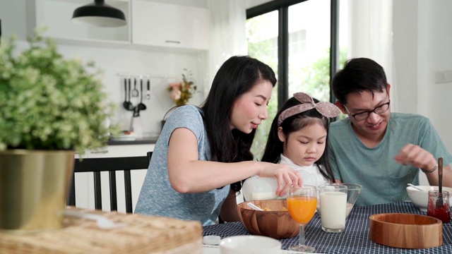 幸福亚洲日本家庭早餐在家。清晨，年轻的父母和女儿在厨房的桌子上吃麦片喝橙汁。品质时刻结合家庭理念理念视频素材