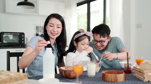 幸福亚洲日本家庭早餐在家。清晨，年轻的父母和女儿在厨房的桌子上吃麦片喝橙汁。品质时刻结合家庭理念理念视频素材