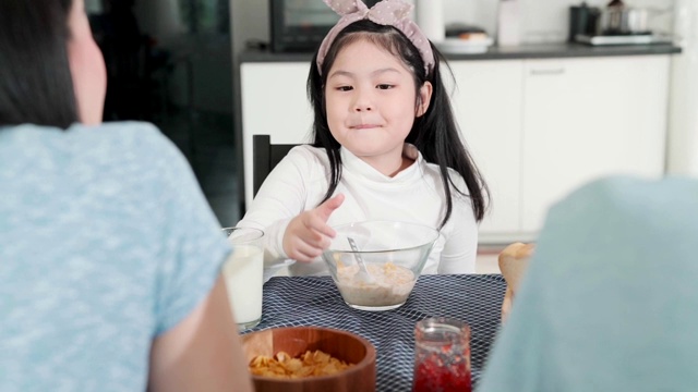 亚洲女性孩子无聊的食物与爸爸妈妈试图说服她吃更多的早餐餐桌上的家庭厨房背景视频素材