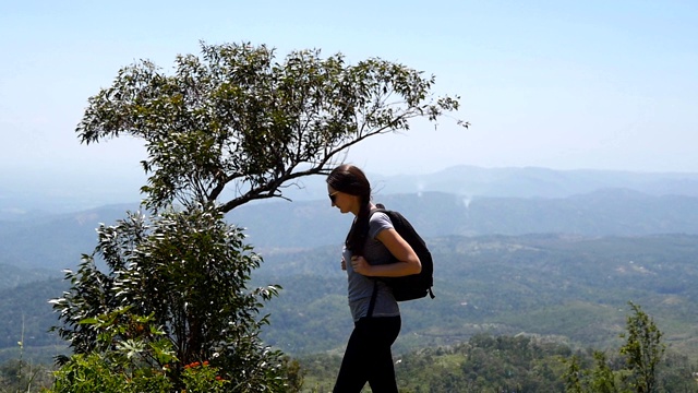 年轻的女性徒步旅行者背包走在小径上的山与峡谷的背景。女游客走在一条小路上，欣赏周围美丽的自然风光。夏季旅游的概念。慢动作视频素材