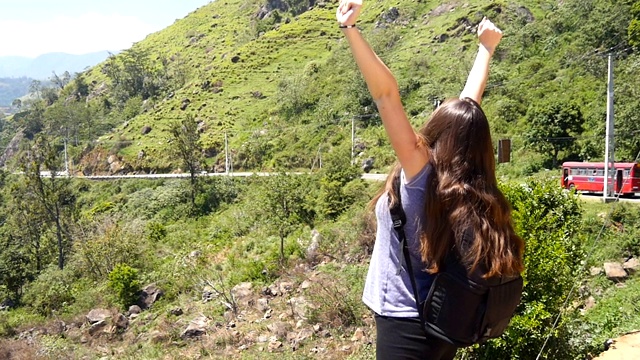 一名背包女游客慢跑到峡谷边缘，举起双手。女性徒步旅行者跑到山顶，伸出手臂。年轻的旅行者欣赏美丽如画的风景。视频素材