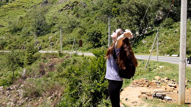 女徒步旅行者背包站在美丽的峡谷边缘，伸出手臂。一名女游客爬上山顶，举起双手。年轻的旅行者喜欢美丽的风景。视频素材