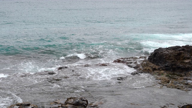 潮汐中的海水猛烈地撞击充满障碍的石质海岸，并撞击水中的岩石，然后分解成60帧/秒的高发生率4k慢动作捕捉视频素材