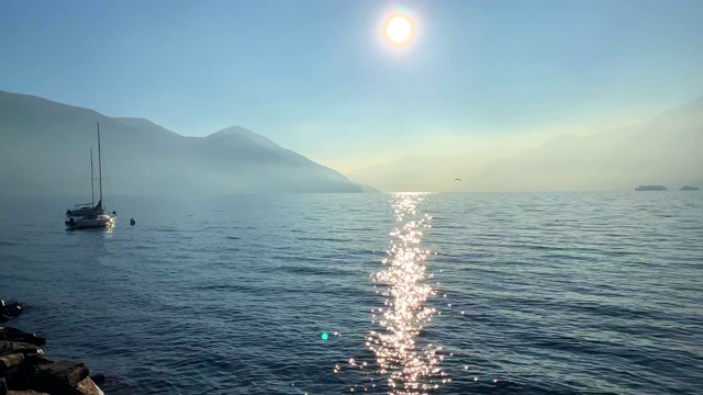 在一个有山和岛屿的高山湖泊上的帆船在一个雾天与阳光视频素材