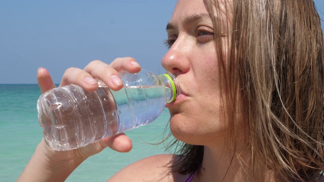 迷人的女人在海滩上喝瓶装饮料水视频素材