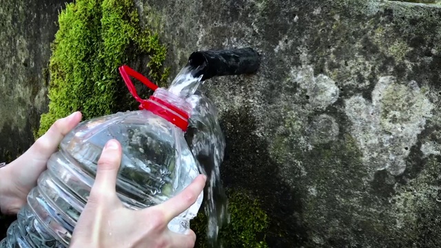 妇女手里拿着塑料水瓶，收集泉水中的淡水。视频素材