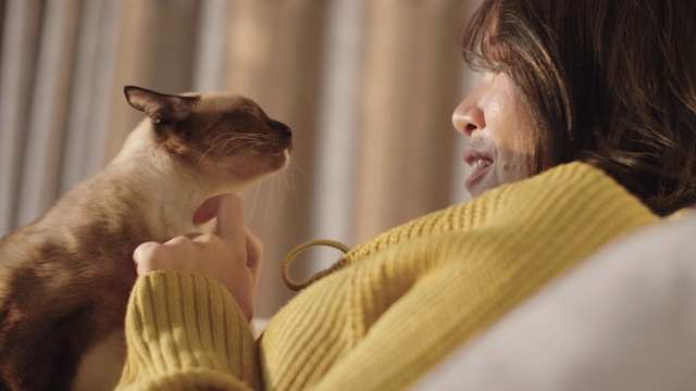 一个女人在卧室的白色床上抚摸她的宠物猫的肖像。视频素材