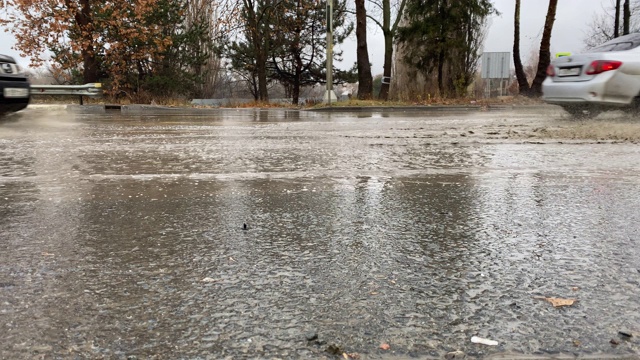 秋天的雨天，城市交通在潮湿的道路上行驶，汽车驶过一个车轮溅起水花的水坑。视频素材