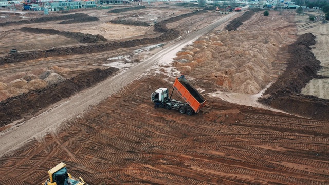 地面为高层公寓建筑准备场地，采石场无人机从沙车拖拉机上泄漏的沙砾用于建造公寓面板房视频素材