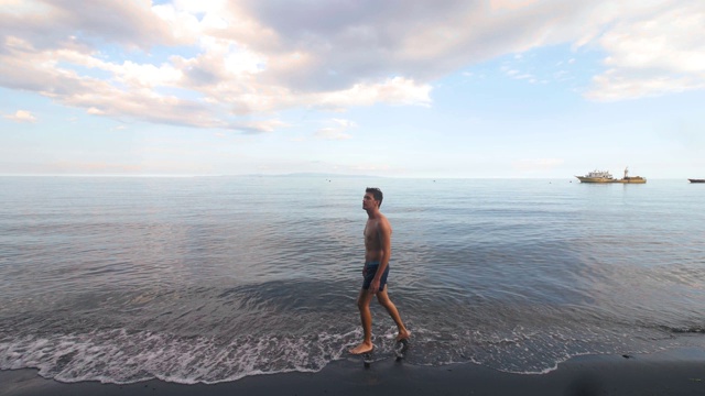 壮汉在夏天在一个炎热的夏天在海滩上来回短距离行走。视频素材