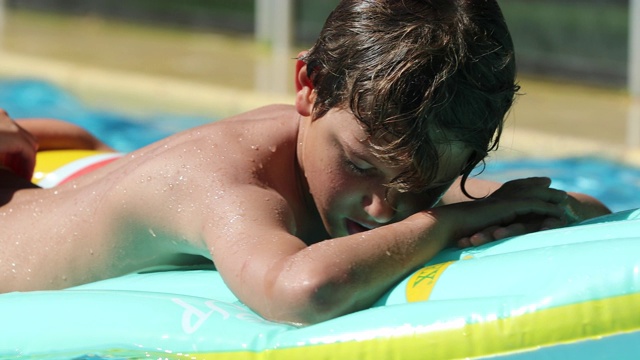 在充气床垫上的泳池边，孩子用舌头挑逗相机放松视频素材