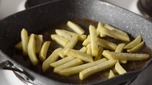 一名男子将新鲜冷冻的生炸薯条土豆片放在热油锅里，用不健康的食物近距离选择性聚焦为自己准备一顿饭视频素材