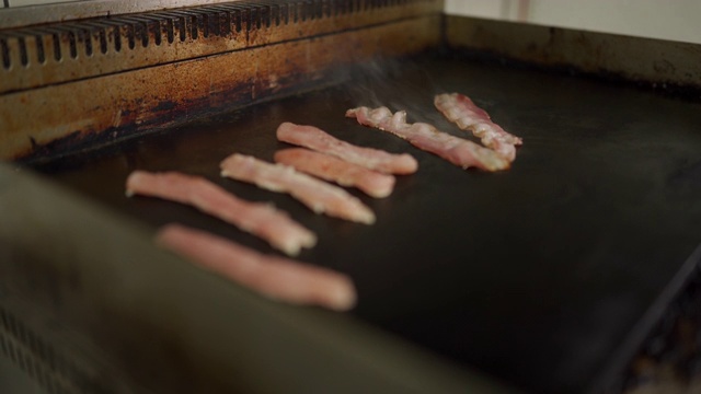 厨师在商业厨房的平顶烤架上烤鸡胸肉和培根片视频素材