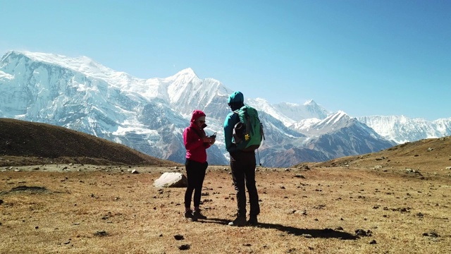 一对夫妇在冰湖上欣赏美景，这是尼泊尔喜马拉雅山Annapurna巡回徒步旅行的一部分。安纳布尔链子在后面，上面覆盖着雪。晴朗的天气，干燥的草地，雪峰。高海拔视频素材