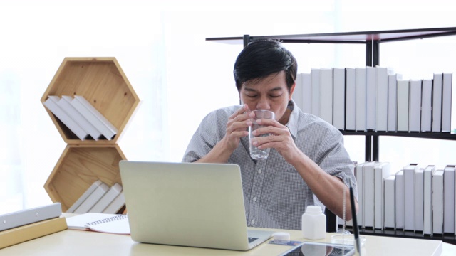 一名年长的亚洲男子使用计算器，努力工作，直到有压力并服用药物视频素材