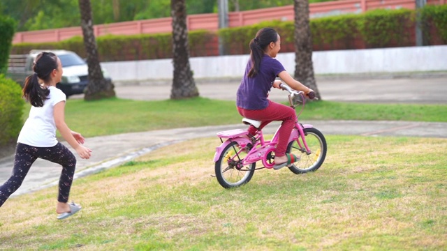 两个亚洲小女孩在花园里骑自行车视频素材