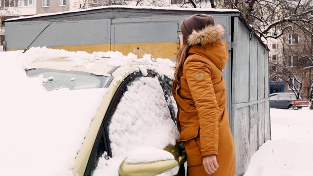 一个穿着暖和夹克的女人在院子里用扫地刷清理撒了雪的沙拉车视频素材