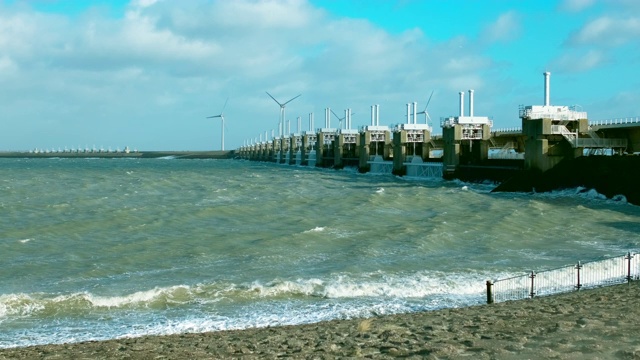 海岸上有风力涡轮机，一道防洪屏障延伸到海里。视频素材