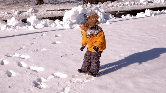 一个小男孩在一个白雪覆盖的公园里玩耍，他在雪地上跳跃和跌倒。视频素材