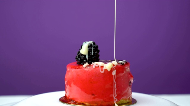 在美味的水果蛋糕上浇上奶油，配上白奶油和黑莓片。紫色的背景视频素材