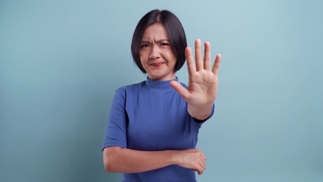 一名愤怒的亚洲妇女看着孤立地站在蓝色背景上的摄像机。4 k的视频视频素材