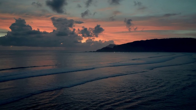 慢动作拍摄的海浪对橙色的天空，在日落时的田园风光的海滩-龙目岛，巴厘岛视频素材