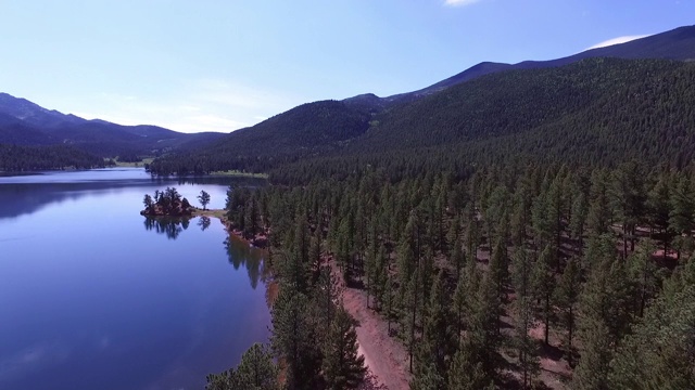 鸟瞰土路在绿树中平静的湖在阳光明媚的一天，风景的山对天空-湖惠灵顿，科罗拉多州视频素材