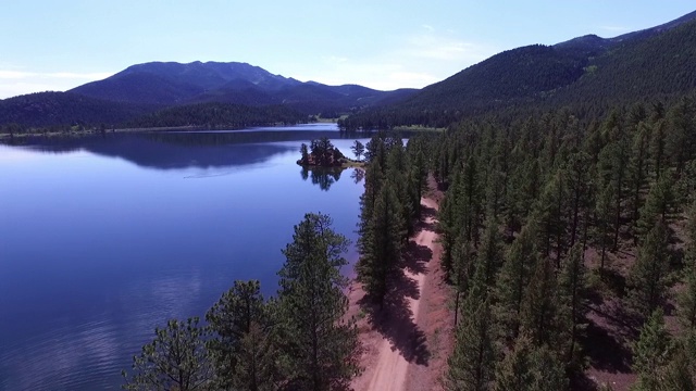 鸟瞰土路在绿树湖边在阳光明媚的一天，风景的山对天空-湖惠灵顿，科罗拉多州视频素材