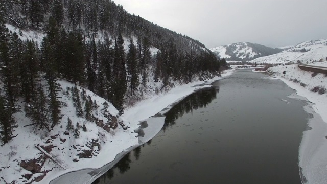 鸟瞰图冰冻的冰原周围的河上的树在雪，无人机向前移动的水在冬季对天空-杰克逊，怀俄明州视频素材