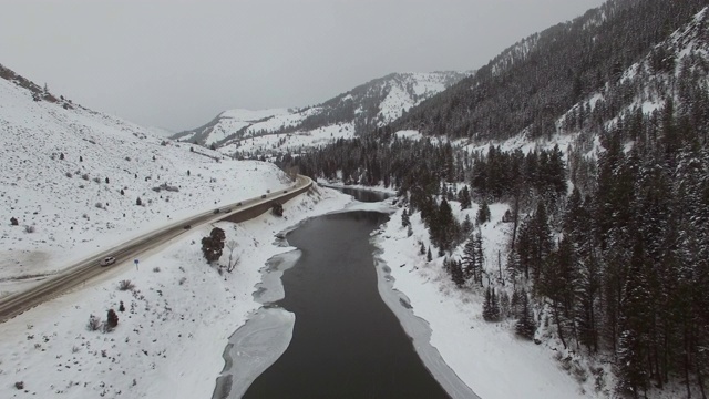 在河流和积雪覆盖的森林道路上的汽车鸟瞰图，无人机向前移动的白色风景对山脉-杰克逊，怀俄明州视频素材