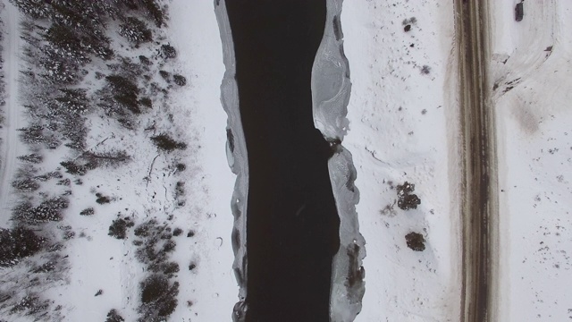 鸟瞰图的河流周围的冰原和雪在冬天，无人机上升在道路上的车辆水上-杰克逊，怀俄明州视频素材