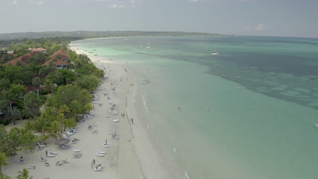 航拍游客在海滩上对着夏天的天空，无人机在棕榈树中海岸与旅游胜地-蒙特哥湾，牙买加视频素材