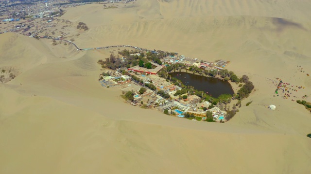 沙丘中建筑物的空中拍摄的绿洲，无人机在沙漠村庄泻湖上移动-瓦卡奇纳，秘鲁视频素材