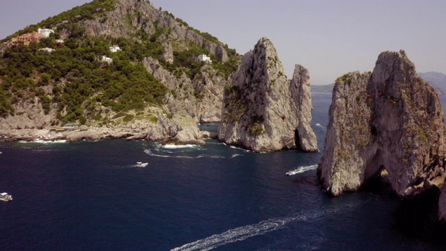 鸟瞰图海鸥飞过海面附近的堆栈岩石在阳光明媚的一天，海鸟移动的水对岩石山-卡普里岛，意大利视频素材