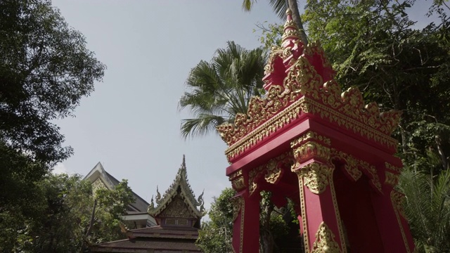 泰国清莱，一个阳光明媚的日子，游客在入口处对着树木拍摄的红色建筑上的金色雕刻视频素材