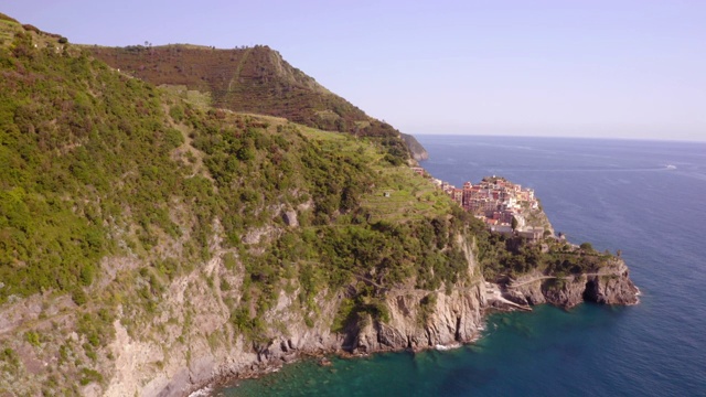 航拍近海悬崖上的沿海城市对天空，无人机在阳光明媚的日子与建筑物水上移动-五Terre，意大利视频素材