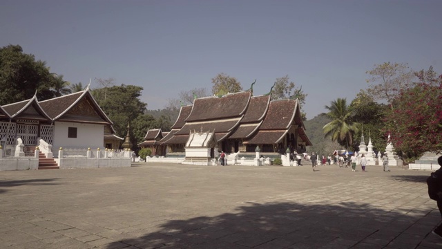 在老挝琅勃拉邦，一个阳光明媚的日子里，游客们在著名的佛教寺庙中对着天空拍摄视频素材