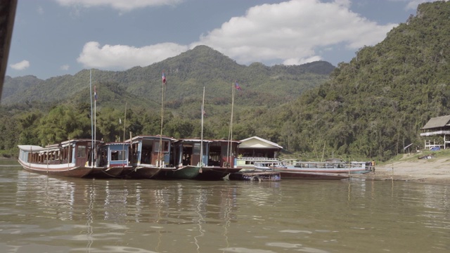 琅勃拉邦，老挝，阳光明媚的一天，用平底船拍摄在河边的绿色山脉上停泊的船只视频素材