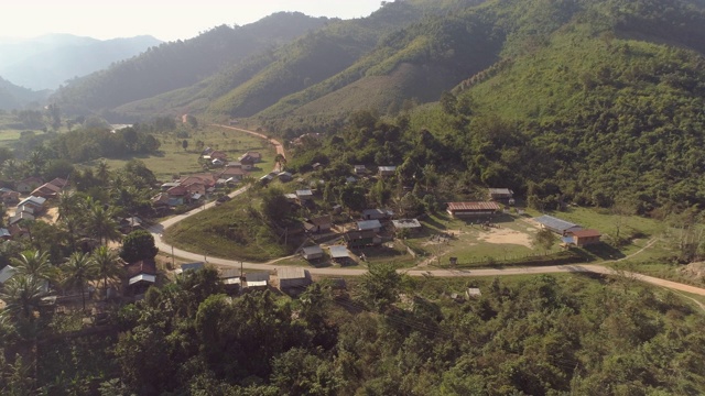 空中拍摄的房子在村庄的绿色山脉，无人机向后飞行山谷在阳光明媚的一天-湄公河，老挝视频素材