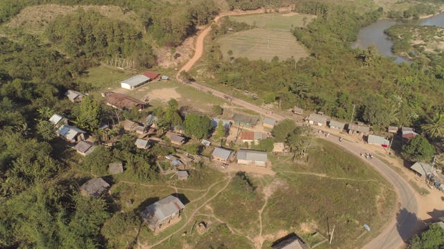 在阳光明媚的日子里，无人机在老挝湄公河流域的住宅建筑上空盘旋，拍摄游客在村庄房屋中间的道路上行走的画面视频素材