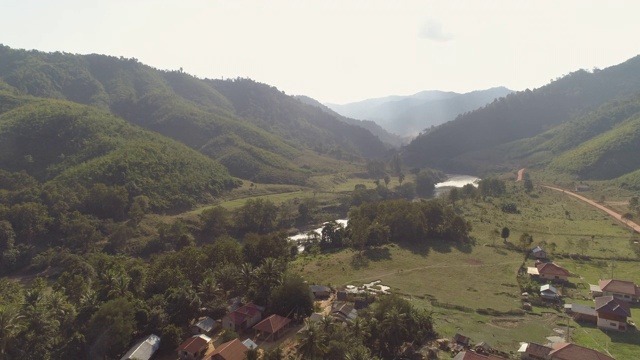 空中拍摄的河流在山谷中村庄附近的树木对天空，无人机向前飞行的房子对山在阳光明媚的一天-湄公河，老挝视频素材