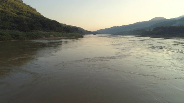 空中拍摄的河流在森林中对天空日落，无人机向前飞行在山间涟漪的水-湄公河，老挝视频素材